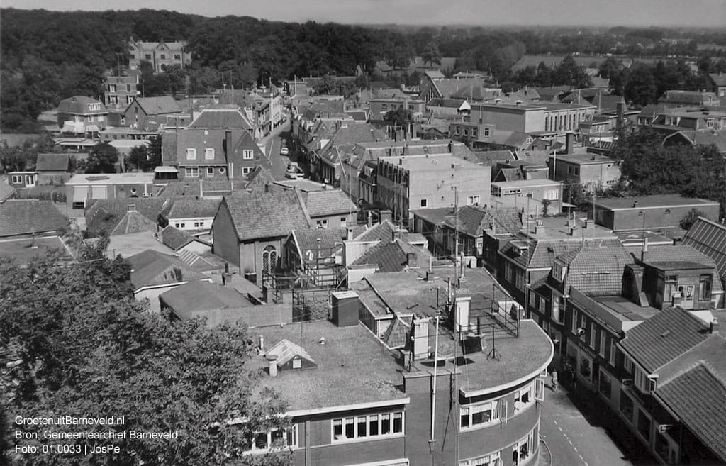 Verleden, 1965 - Foto vanaf de toren van de Oude Kerk. Iets links vanaf het midden voormalige synagoge (tegenwoordig Kaasschieter Optiek) aan de Jan van Schaffelaarstraat. Op de achtergrond Huize De Schaffelaar. - Barneveld