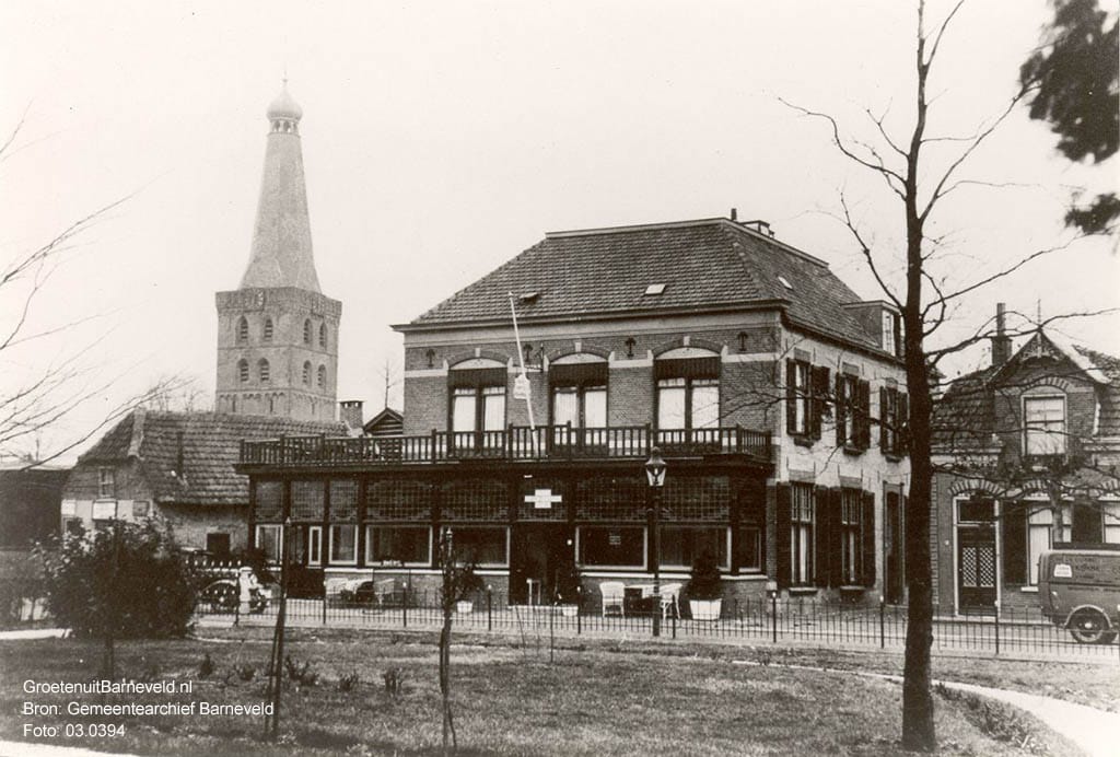 Verleden 1930/1940 - De foto is gemaakt vanuit de tuin van de Westerveldstichting met in het midden Hotel Café Restaurant Hof van Gelderland. Links van het hotel het pand van Tolboom. Rechts het huis van Van den Berg?. Op de achtergrond de toren van de Oude Kerk. - Barneveld