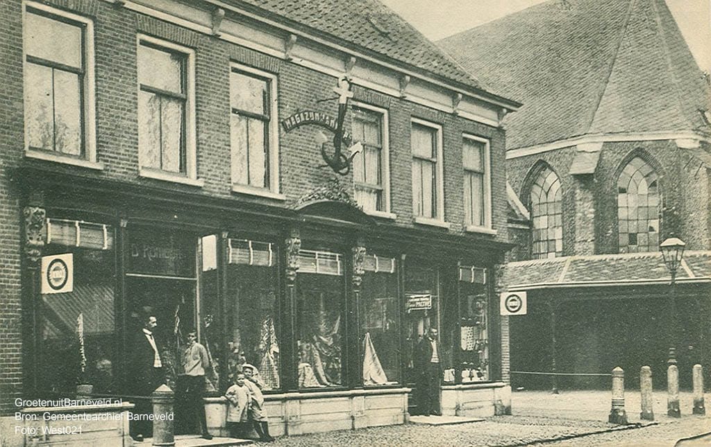 Verleden 1910/1925 - Magazijn 't Anker van de firma D. Romeijn, Manufacturen en bedden. Rechts de Oude Kerk met de overkapping van de botermarkt. - Barneveld
